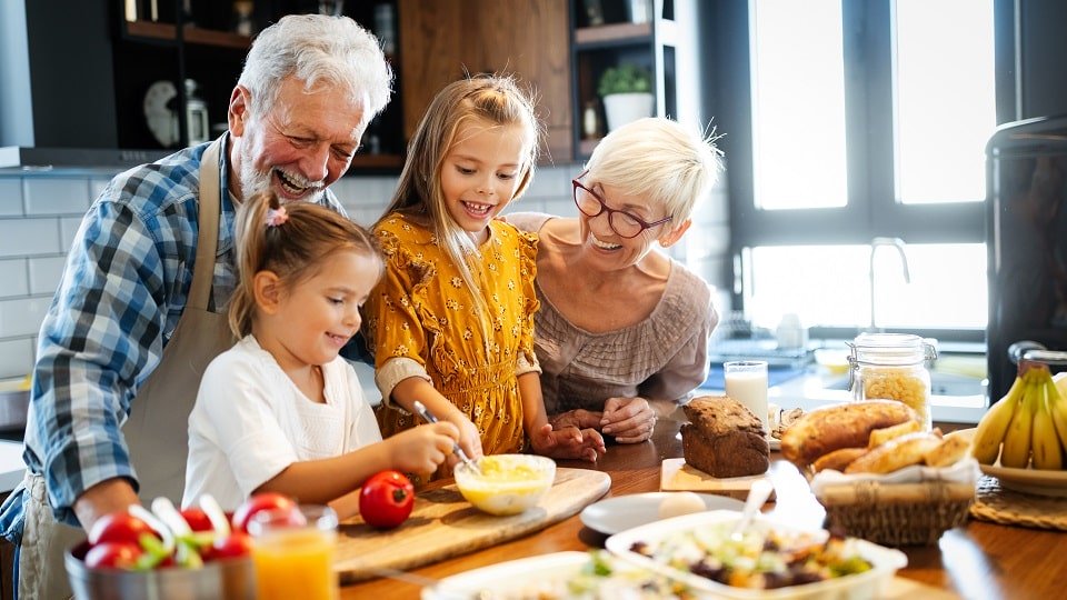 Des grands-parents et leurs petits-enfants préparant un repas dans une cuisine lumineuse.