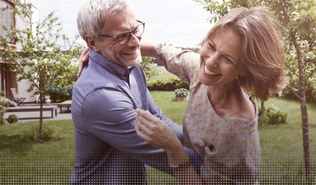 Un couple souriant danse dans un jardin verdoyant.