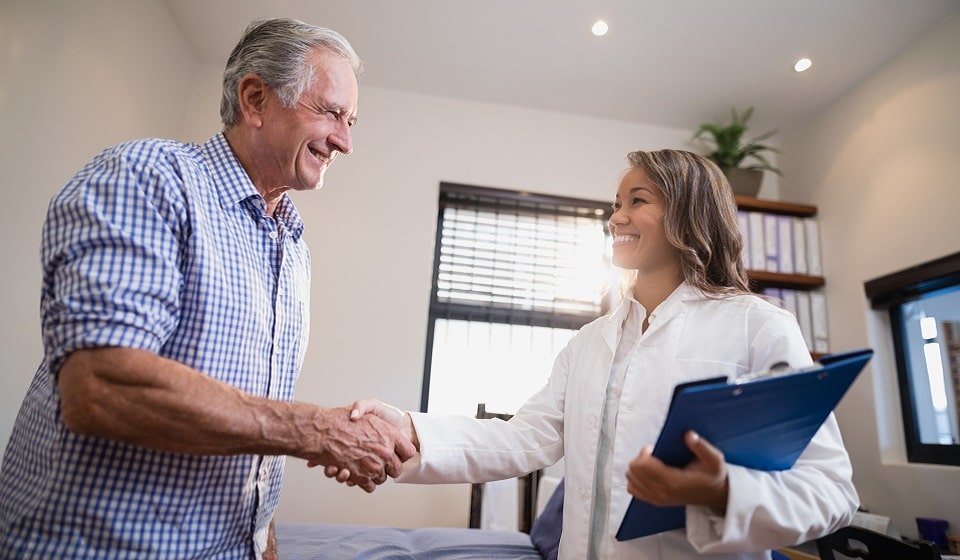 Audioprothésiste accueillant chaleureusement un client dans un cabinet de soins auditifs.