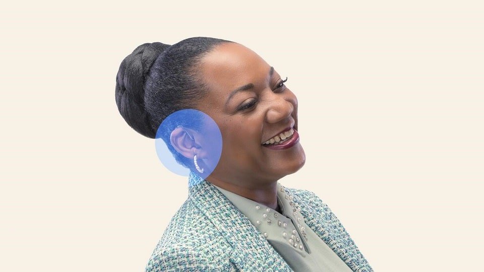 Une femme portant un appareil auditif sourit.