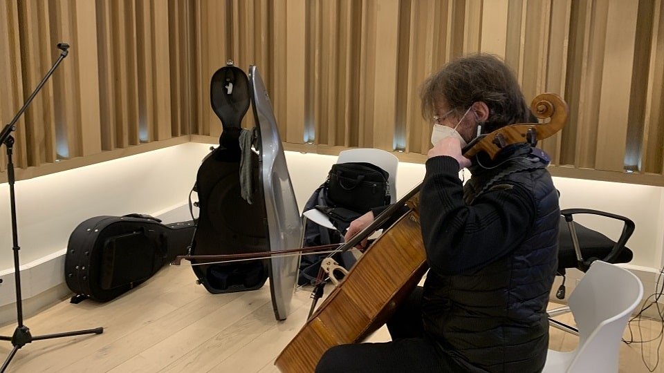 un violoncelliste jouant dans une cabine à musique avec des étuis et des accessoires posés au sol