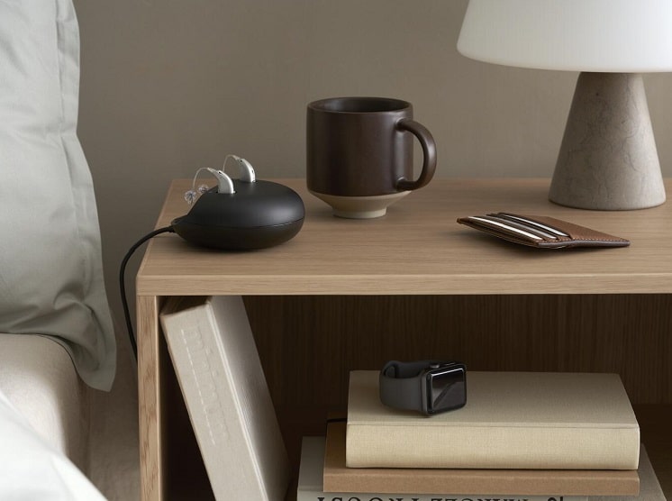 Les appareils auditifs dans leur station de charge sur une table de nuit à côté du lit