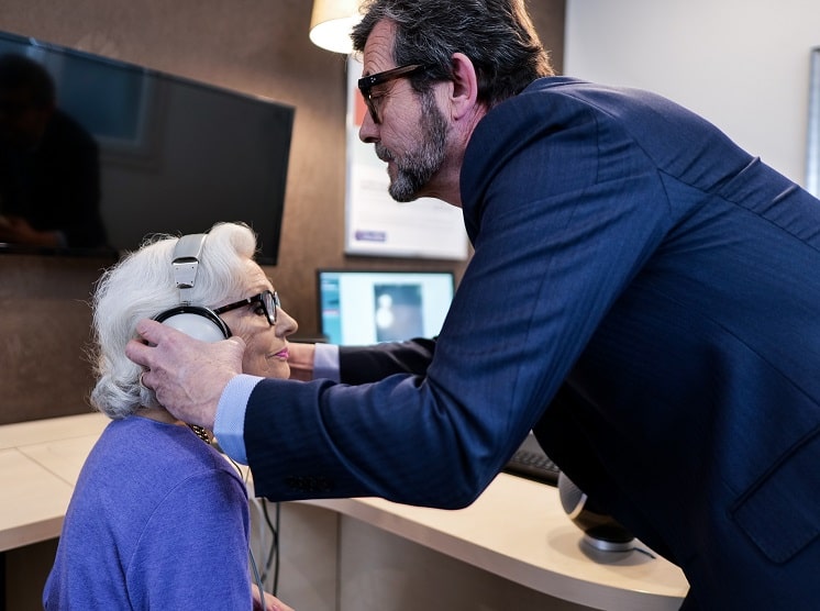 Un audioprothésiste qui pose le casque sur les oreilles d'une cliente Audika afin de passer le test auditif