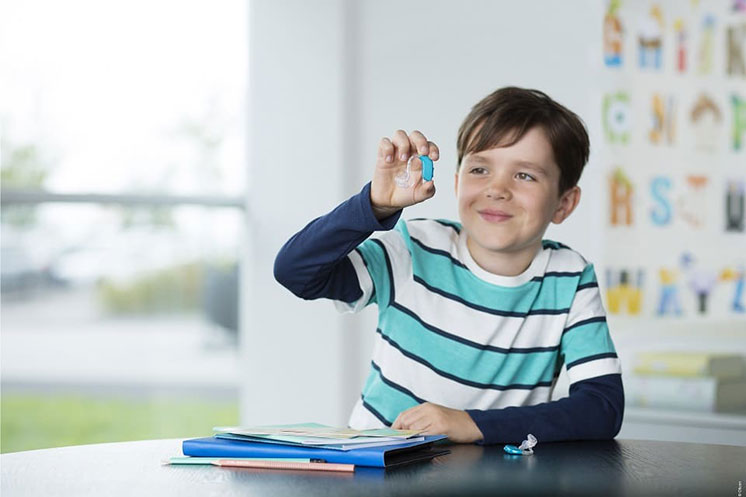 Un enfant montre une aide auditive dans une salle lumineuse.