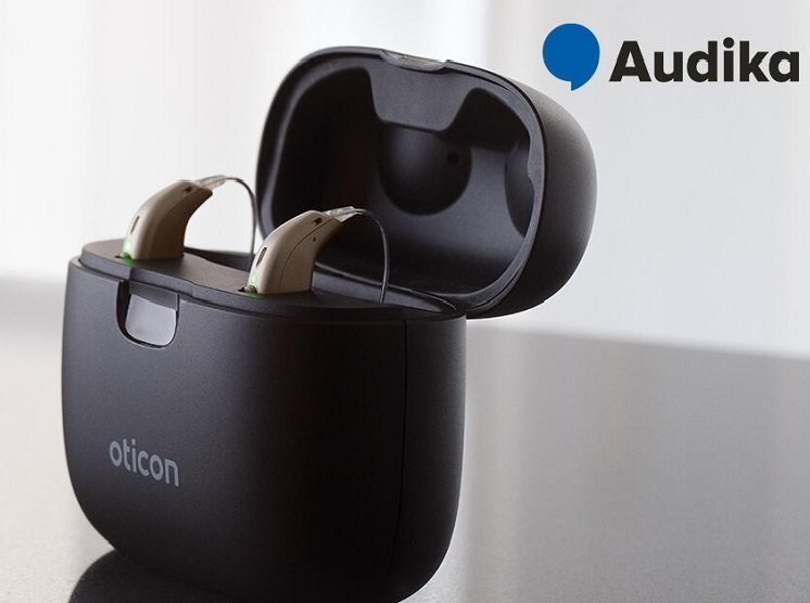 Appareils auditifs rechargeables Oticon dans un boîtier de charge avec logo Audika.