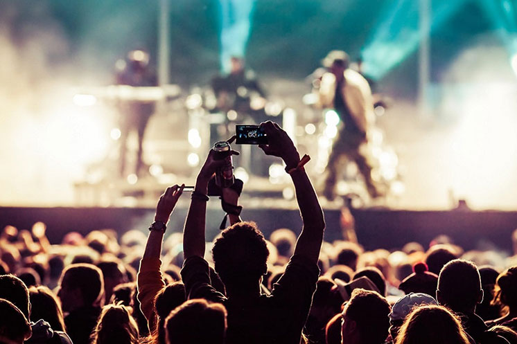 Une foule de personnes assistent à un concert avec une scène éclairée en arrière-plan.