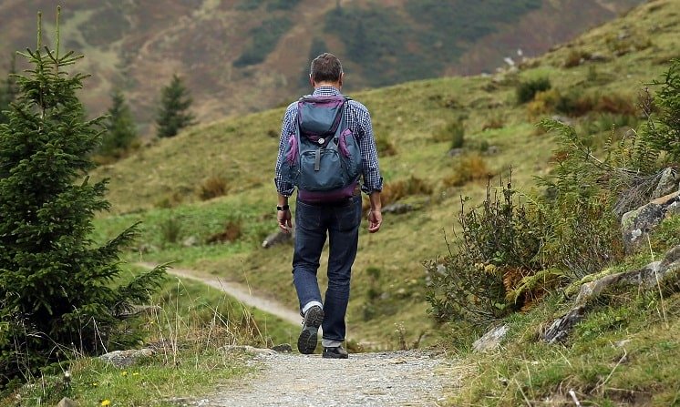 Un homme marche sur un sentier de montagne entouré de verdure.