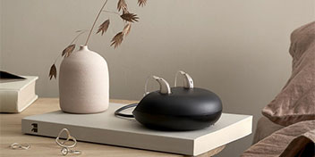 Appareils auditifs rechargeables posés sur une table, avec un décor minimaliste en arrière-plan