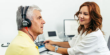 Homme portant un casque auditif passant un test auditif avec une audioprothésiste