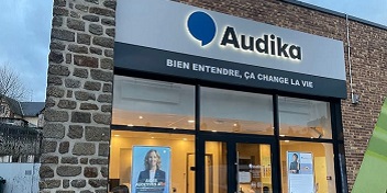 Devanture du centre auditif Audika La Ferté-Macé avec enseigne lumineuse et affiches publicitaires en vitrine.