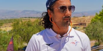 Entretien avec Romain, athlète de la FFTir, portant un polo blanc sur un terrain ensoleillé.