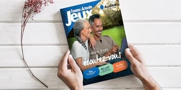 Magazine de jeux Audika posé entre les mains, avec une couverture mettant en avant l’audition et le bien-être.