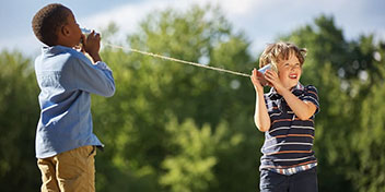 Deux enfants communiquent avec un téléphone en gobelets dans un parc