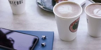 Appareils auditifs discrets à côté d’un smartphone et de tasses de café sur une table