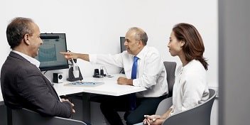 Un couple consulte un audioprothésiste qui explique des résultats d’audiogramme sur un écran.