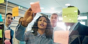 Une séance de brainstorming en entreprise avec des professionnels appareillés collaborant devant un tableau de notes adhésives.