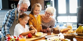 Des grands-parents équipés d’aides auditives cuisinant avec leurs petits-enfants dans une cuisine lumineuse.