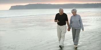 Couple âgé marchant sur la plage au coucher du soleil, discutant de la santé auditive.