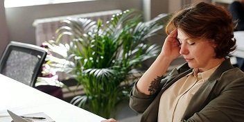 Femme souffrant d'acouphènes, tenant sa tête avec une expression de douleur, dans un environnement professionnel.