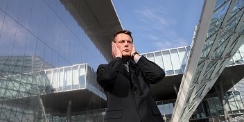 Homme en costume souffrant de bruit dans un quartier moderne avec des bâtiments en verre.