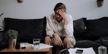 Une femme assise sur un canapé tient sa tête, manifestant une gêne liée à des acouphènes.