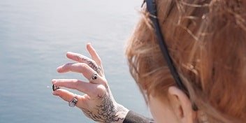 Une femme tatouée aux cheveux roux tenant des appareils auditifs intra-auriculaires devant un arrière-plan bleu.