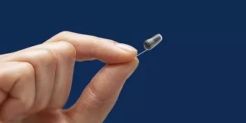 Une main féminine tient un appareil auditif invisible contre un fond bleu.