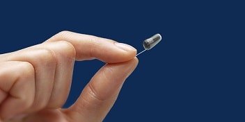 Une main féminine tient un appareil auditif invisible contre un fond bleu.