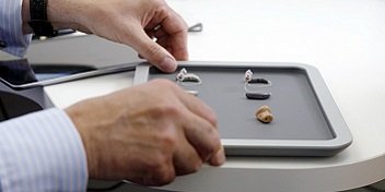 Plateau contenant divers modèles d’appareils auditifs manipulés par une personne.