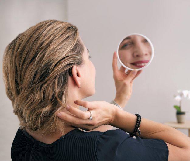 Une femme se regardant dans le miroir et portant des appareils auditifs mini contours 