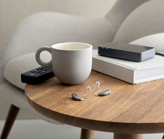 Des appareils auditifs mini contours posés sur une table basse avec une tasse à café