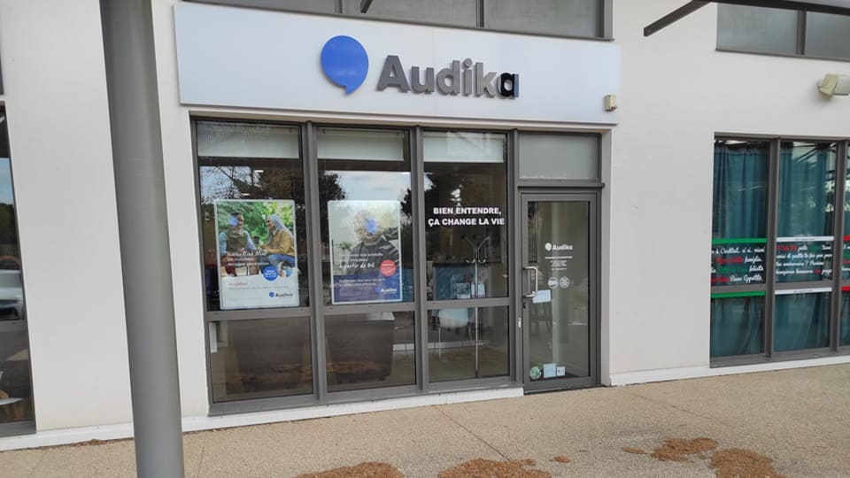La façade d’une clinique Audika, spécialisée en soins auditifs, affiche le slogan « Bien entendre, ça change la vie. » et des affiches promotionnelles sur les tests et appareils auditifs.