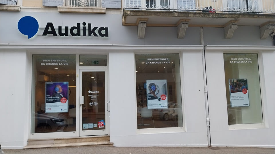 La façade d’une clinique Audika affiche des publicités et le slogan 'Bien entendre, ça change la vie' sur ses vitrines. L’entrée centrale mène à des services d’audiologie.