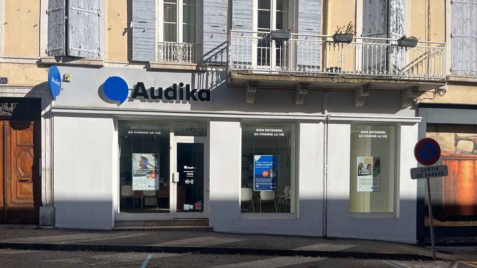 La façade d’une clinique Audika affiche des publicités et le slogan ’Bien entendre, ça change la vie’ sur ses vitrines. L’entrée centrale mène à des services d’audiologie.
