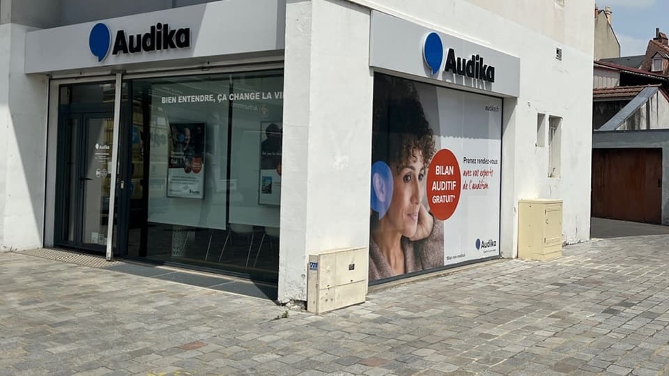 La façade d'une clinique Audika affiche le logo bleu et blanc, avec une vitrine invitant à un 'Bilan Auditif Gratuit'. Slogan visible : 'Bien entendre, ça change la vie'.