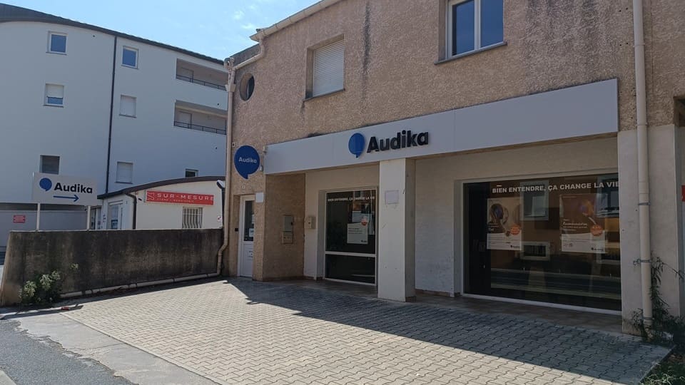 La façade d'une clinique Audika spécialisée dans les soins auditifs affiche le slogan « Bien entendre, ça change la vie ». L'entrée est entourée d'immeubles résidentiels modernes.
