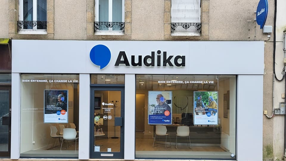 La façade d’une clinique Audika, spécialisée en santé auditive, affiche le slogan « Bien entendre, ça change la vie » et des posters promouvant tests auditifs et prothèses auditives.