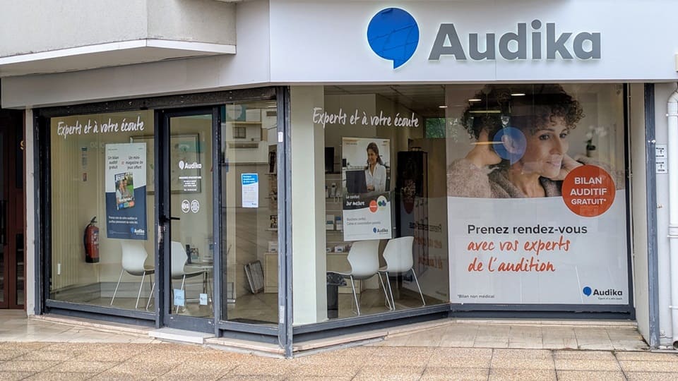 Façade d’un centre Audika dans un environnement urbain, affichant les slogans « Experts de l’audition à votre écoute ». Vitrine annonçant « Bilan auditif gratuit » avec prise de rendez-vous pour expertise en audition.