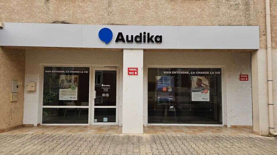 La façade d’une clinique Audika spécialisée dans les soins auditifs affiche le slogan « Bien entendre, ça change la vie ». L’entrée est entourée d’immeubles résidentiels modernes.