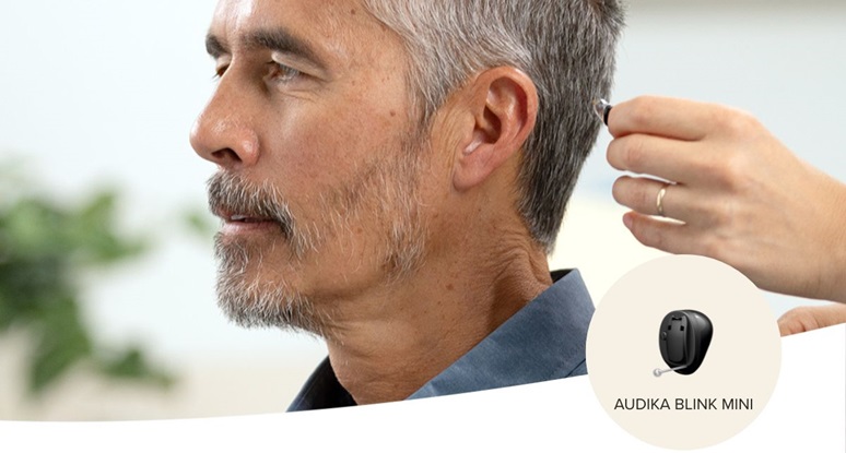 Une main plaçant une aide auditive Audika Blink Mini dans l’oreille d’une personne.