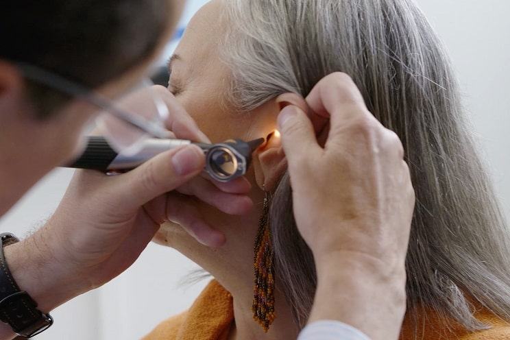 Audioprothésiste effectuant un examen de l’oreille d’une femme avec des symptômes d’acouphènes.