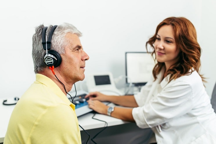Un patient porte un casque tandis qu’un audioprothésiste effectue un test auditif dans un cabinet médical.