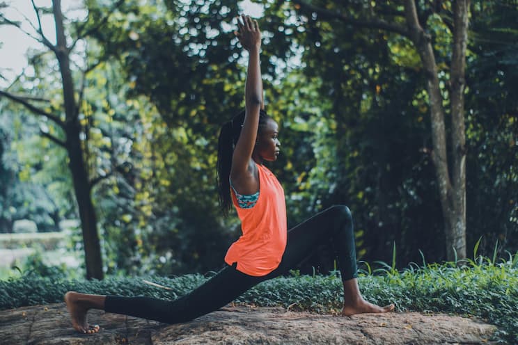 Jeune femme pratiquant une posture de yoga en plein air dans un cadre naturel verdoyant.