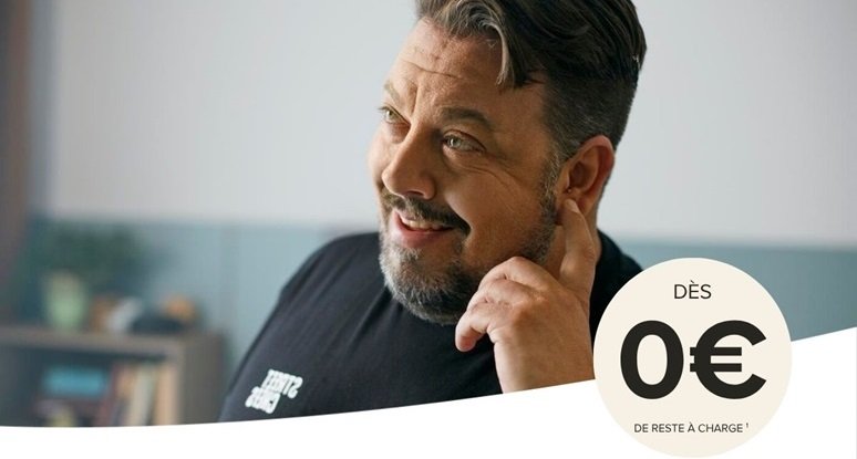 Homme souriant portant un appareil auditif et touchant son oreille, avec un texte indiquant ’Dès 0€ de reste à charge’.