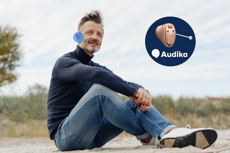Un homme assis dehors portant des appareils auditifs Audika presque invisibles.