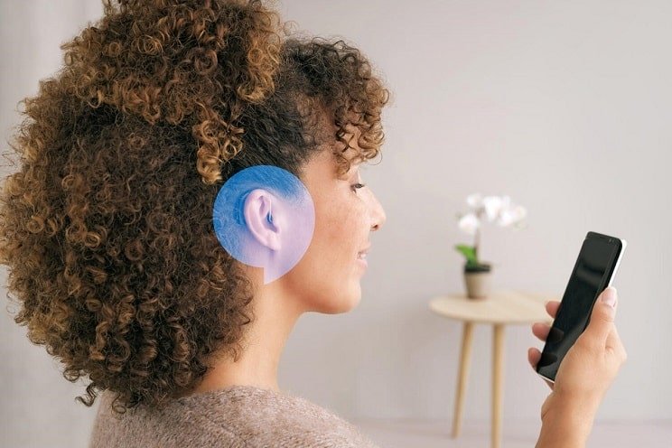 Femme portant des appareils auditifs Bluetooth et utilisant un smartphone.