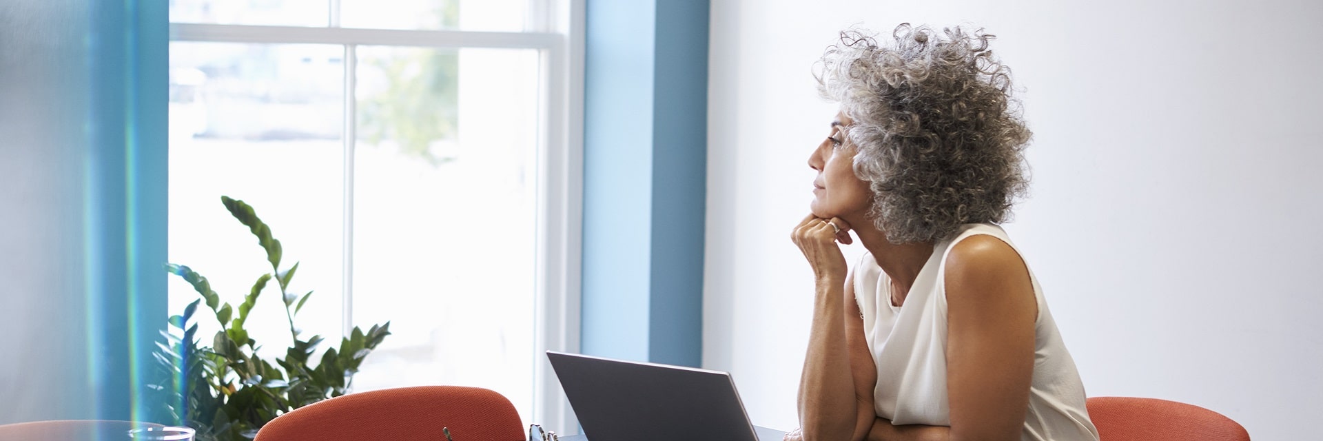 Femme pensive regardant par la fenêtre devant un ordinateur