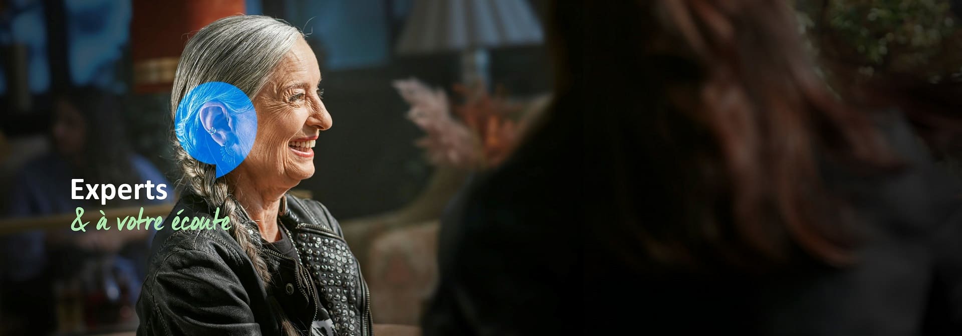 Un audioprothésiste Audika conseille une femme portant un appareil auditif, avec le texte « Experts à votre écoute » affiché.