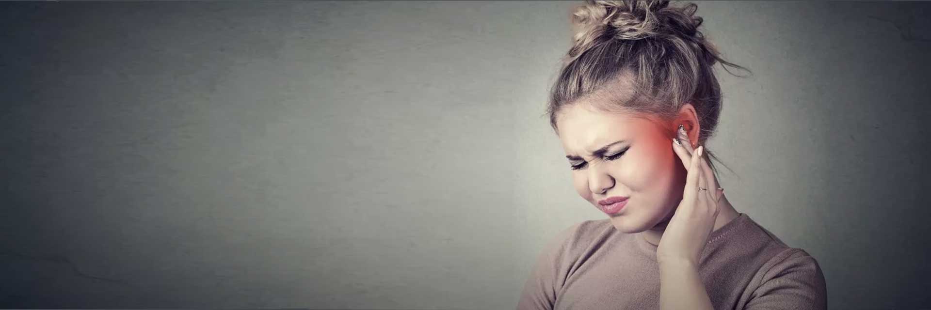 Une jeune femme touche son oreille avec une expression d'inconfort.