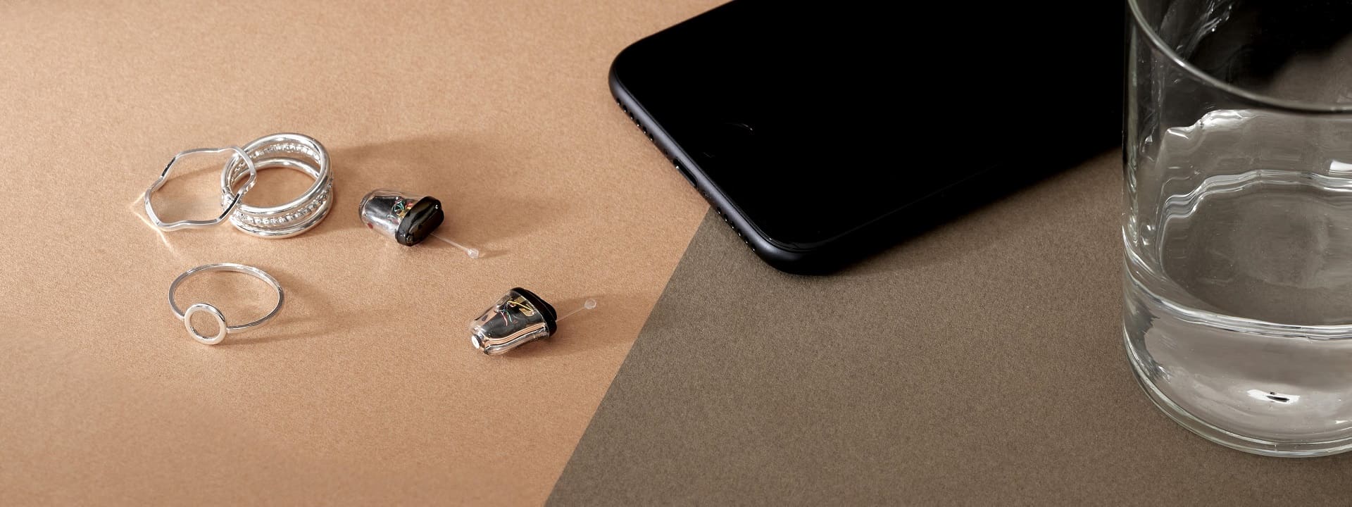 Appareils auditifs invisibles déposés à côté de bijoux et d'un mobile